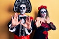 Young couple wearing mexican day of the dead costume over yellow moving away hands palms showing refusal and denial with afraid