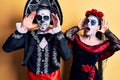 Young couple wearing mexican day of the dead costume over yellow smiling cheerful playing peek a boo with hands showing face