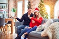 Young couple wearing santa claus hat sitting on the sofa around christmas tree at home amazed and smiling to the camera while Royalty Free Stock Photo