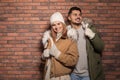 Young couple wearing warm clothes against wall, space for text. Ready for winter vacation