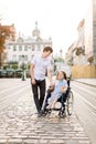 Young Couple In Wheelchair Strolling In old City. Lovely couple, woman in wheelchair and her husband, walking outdoors Royalty Free Stock Photo
