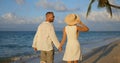 Young couple in white clothes enjoying tropical sunset on the sandy beach by walking hand in hand Royalty Free Stock Photo
