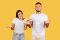 A young couple in white t-shirts shrugging with their palms up