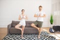 Young couple in white tshirts doing yoga at home standing in tree pose Royalty Free Stock Photo