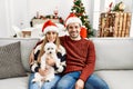 Young couple of wife and husband sitting on the sofa wearing christmas hat at home looking positive and happy standing and smiling Royalty Free Stock Photo