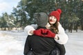 Young couple on winter forest background, girl keeps hands in heart shape sign. Winter sunny day