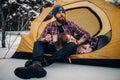 Young couple in tourist tent during winter hike. Guy drinks hot tea from metal mug, girl lies. Royalty Free Stock Photo