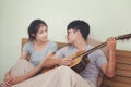 Young couple, young man playing guitar in a relaxing holiday room. Royalty Free Stock Photo