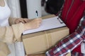 Young courier delivery man in red uniform holding a parcel cardboard box delivering package and woman putting signature in Royalty Free Stock Photo