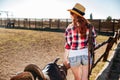 Young cowgirl in straw hat preparing saddle for a ride