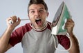 Young crazy desperate and frustrated man doing housework holding iron