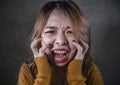 Young crazy desperate and upset Asian Korean woman screaming scared and anxious feeling anger and pain isolated on dark background