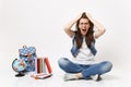 Young crazy dizzy woman student in denim clothes screaming clinging to head sitting near globe, backpack school books