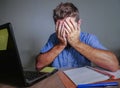 Young crazy stressed and overwhelmed man working messy at office desk desperate with laptop computer covering face with hands frus Royalty Free Stock Photo