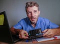 Young crazy stressed and overwhelmed man working messy at office desk desperate with laptop computer feeling frustrated using calc Royalty Free Stock Photo