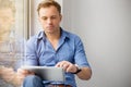 Young creative man sitting at window and using tablet computer Royalty Free Stock Photo