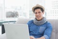 Man wearing straw hat, gray scarf sitting on sofa by windows using laptop, copy space Royalty Free Stock Photo