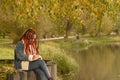 Young creative woman with dreadlocks drawing, writing in notebook, sitting on stumps near lake in parkland. Royalty Free Stock Photo