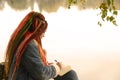 Young creative woman with dreadlocks drawing, writing in notebook, sitting on stumps near lake in parkland. Royalty Free Stock Photo
