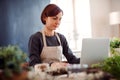 Young creative woman in a flower shop, using laptop. A startup of florist business. Royalty Free Stock Photo