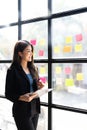 Young creative woman professional using sticky notes in glass wall to writing strategy business plan to development grow Royalty Free Stock Photo