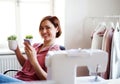 Young creative woman in a studio, using smartphone. A startup of tailoring business. Royalty Free Stock Photo