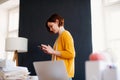 Young creative woman in a studio, using smartphone. A startup of tailoring business. Royalty Free Stock Photo