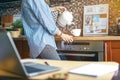 Young cropped woman preparing tea at wooden table in kitchen. Pouring water into a cup from kettle before job. Distance learning Royalty Free Stock Photo