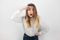 Young curious blond woman holding her hand near her forehead gazing out standing on isolated white background