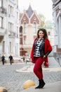 Young curled girl weared in black leather jacket and red scarf on background of old City