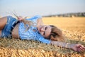 Young curly blond woman, wearing jeans shorts and light blue shirt, lying on bale on field in summer. Close-up female portrait in Royalty Free Stock Photo