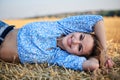 Young curly blond woman, wearing jeans shorts and light blue shirt, lying on bale on field in summer. Close-up female portrait in Royalty Free Stock Photo