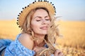 Young curly blond woman, wearing jeans shorts, light blue shirt and straw hat, lying on field in summer. Close-up Female portrait Royalty Free Stock Photo