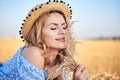 Young curly blond woman, wearing jeans shorts, light blue shirt and straw hat, lying on field in summer. Close-up Female portrait Royalty Free Stock Photo