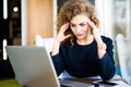 Young curly businesswoman suffering from headache in front of laptop at office desk in modern office Royalty Free Stock Photo