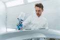 Young curly car painter varnishes a car bumper. Man works in a spray booth. Process of painting car body parts. Royalty Free Stock Photo