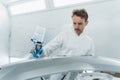 Young curly car painter varnishes a car bumper. Man works in a spray booth. Process of painting car body parts. Royalty Free Stock Photo