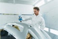 Young curly car painter varnishes a car bumper. Man works in a spray booth. Royalty Free Stock Photo