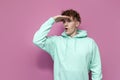 young curly guy student in mint hoodie looks into the distance beyond the horizon on pink isolated background