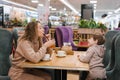 Young curly haired mother and her little son are having breakfast or lunch in a cafe, sitting at a table. Family weekend Royalty Free Stock Photo