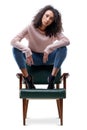 Young woman poses confidently on chair, curly hair, pink sweater Royalty Free Stock Photo