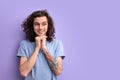 Young curly male in blue t-shirt, with a crafty expression that he came up with,keeping hands together