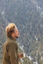 Young curly male tourist climber blond stands on the background of a pine forest in the snow on the slope of the Himalayas and hol