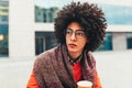 Young curly mixed-race boy drinks coffee on the street against the background of office buildings. Youth culture and fashion. Royalty Free Stock Photo