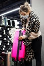 Young customer in casual clothes, mask and leopard scarf is opening locks in bright pink suitcase in supermarket. Trips topandemic Royalty Free Stock Photo