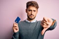 Young customer man with beard holding credit card for payment over pink background with angry face, negative sign showing dislike Royalty Free Stock Photo