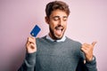 Young customer man with beard holding credit card for payment over pink background pointing and showing with thumb up to the side Royalty Free Stock Photo