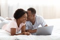 Young cute african couple using laptop while resting in bed