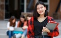 Young and cute Asian college student girls holding books, pose to camera with group of friends blur in background in front of Royalty Free Stock Photo