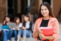 Young and cute Asian college student girls holding books, pose to camera with group of friends blur in background in front of Royalty Free Stock Photo